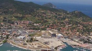 Sopra una veduta aerea dell’area portuale destinata alla realizzazione del Porto Cantieri, a sinistra il piazzale del cantiere Esaom a Portoferraio