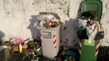 Un cestino al cimitero circondato dai rifiuti