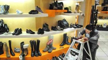 Sopra una commessa applica il cartellino a un paio di scarpe A lato il comandante dei vigili urbani Oliviero Billi