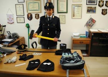 Una poliziotta mostra la mazza di ferro utilizzata per abbattere le porte, sul tavolo gli altri attrezzi