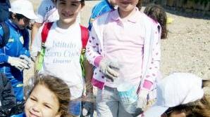 A fianco e sotto i bambini mostrano i rifiuti trovati sulle spiagge e messi nei sacchetti