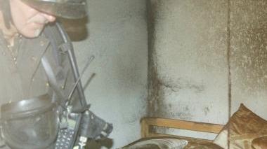A sinistra i vigili del fuoco mentre terminano le operazioni di bonifica nella stanza incendiata. Sopra uno dei pompieri mentre entra nella palazzina di via Santo Stefano dove è divampato l’incendio e a destra una foto del salotto, le cui pareti sono state danneggiate dal fumo.