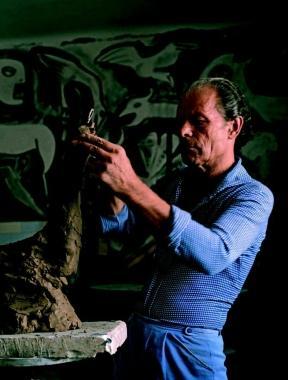 Agenore Fabbri nel suo studio mentre modella la creta di una piccola scultura  