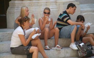 Turisti che consumano un panino e sotto Roberto Isola, titolare di un negozio di delicatezze  