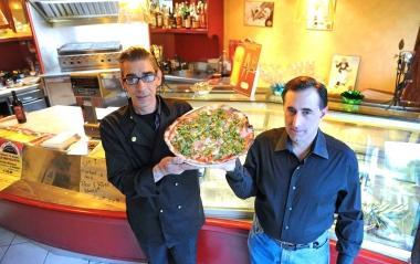 Due gestori del locale mostrano una delle pizze ultra sottili 