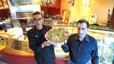 Due gestori del locale mostrano una delle pizze ultra sottili