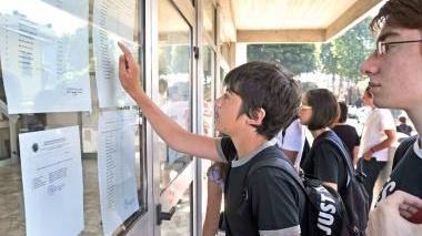 Risultati degli scrutini: studenti osservano i cartelloni in una scuola superiore