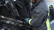 Un vigile del fuoco davanti a un’auto distrutta da un incendio