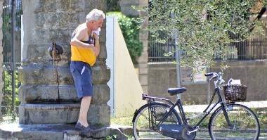 Un anziano si rinfresca a una fontanella pubblica prima di ripartire con la bici  