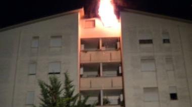 Le fiamme escono dalla mansarda A destra, due residenti “sfollati” e alle loro spalle il palazzo con l’appartamento bruciato all’ultimo piano