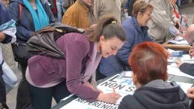 Una giovane mette la firma ad un banchino organizzato al mercato