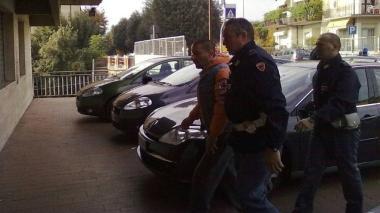 Gianluca Biagianti viene riportato in questura dopo la perquisizione domiciliare dagli uomini della Volante. A fianco la porta della Farmacia Banci con il vetro rotto