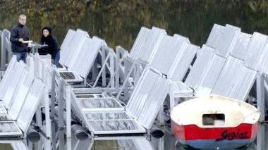 Un tecnico spiega il progetto, mentre in alto si possono vedere i pannelli sull’acqua del laghetto