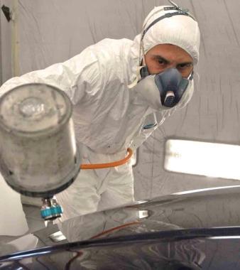 Carrozziere al lavoro e, a sinistra, operaio in officina 