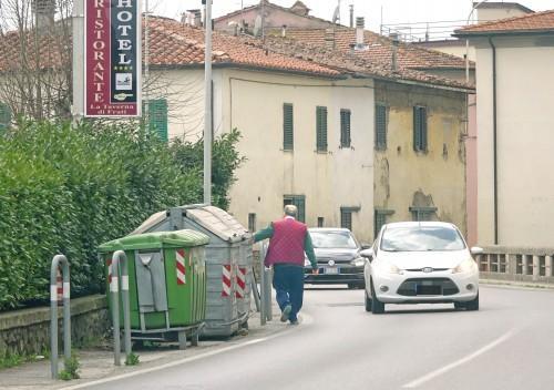 Cassonetti in una curva pericolosa, con un pedone costretto a passare a pochi centimetri dalle auto in assenza di marciapiedi in uno dei tratti più pericolosi di via Sestini a Spazzavento