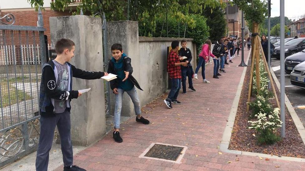 La catena umana degli studenti della media che si passano i libri da collocare nella nuova biblioteca