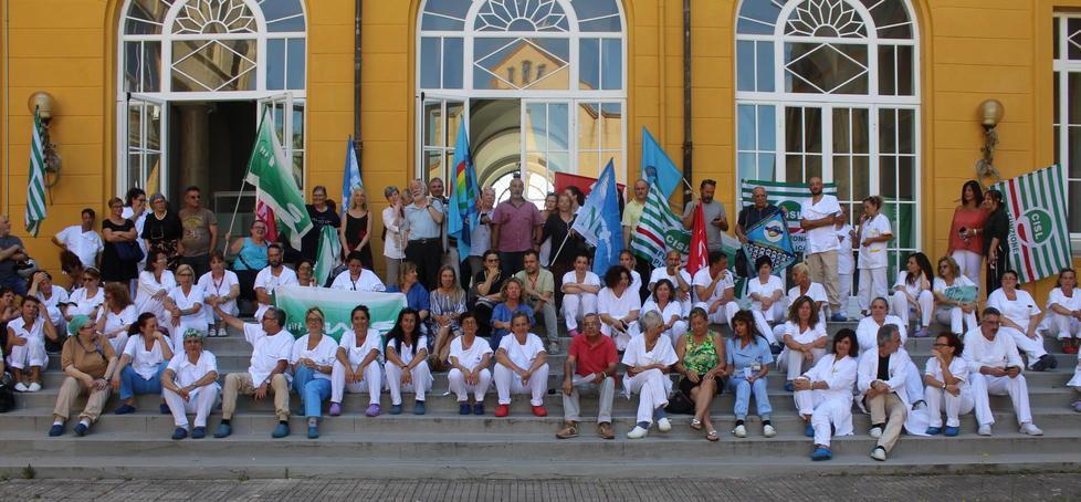 L’azienda ha negato il permesso di utilizzare la sala per fare l’assemblea organizzata dal fronte sindacale (poi verrà offerta la sala Ceccarini): i dirigenti sindacali e i lavoratori polemicamente spostano la riunione nel giardino dell’ospedale per mostrare in modo ironico lo stato dei rapporti fra lavoratori e direzione