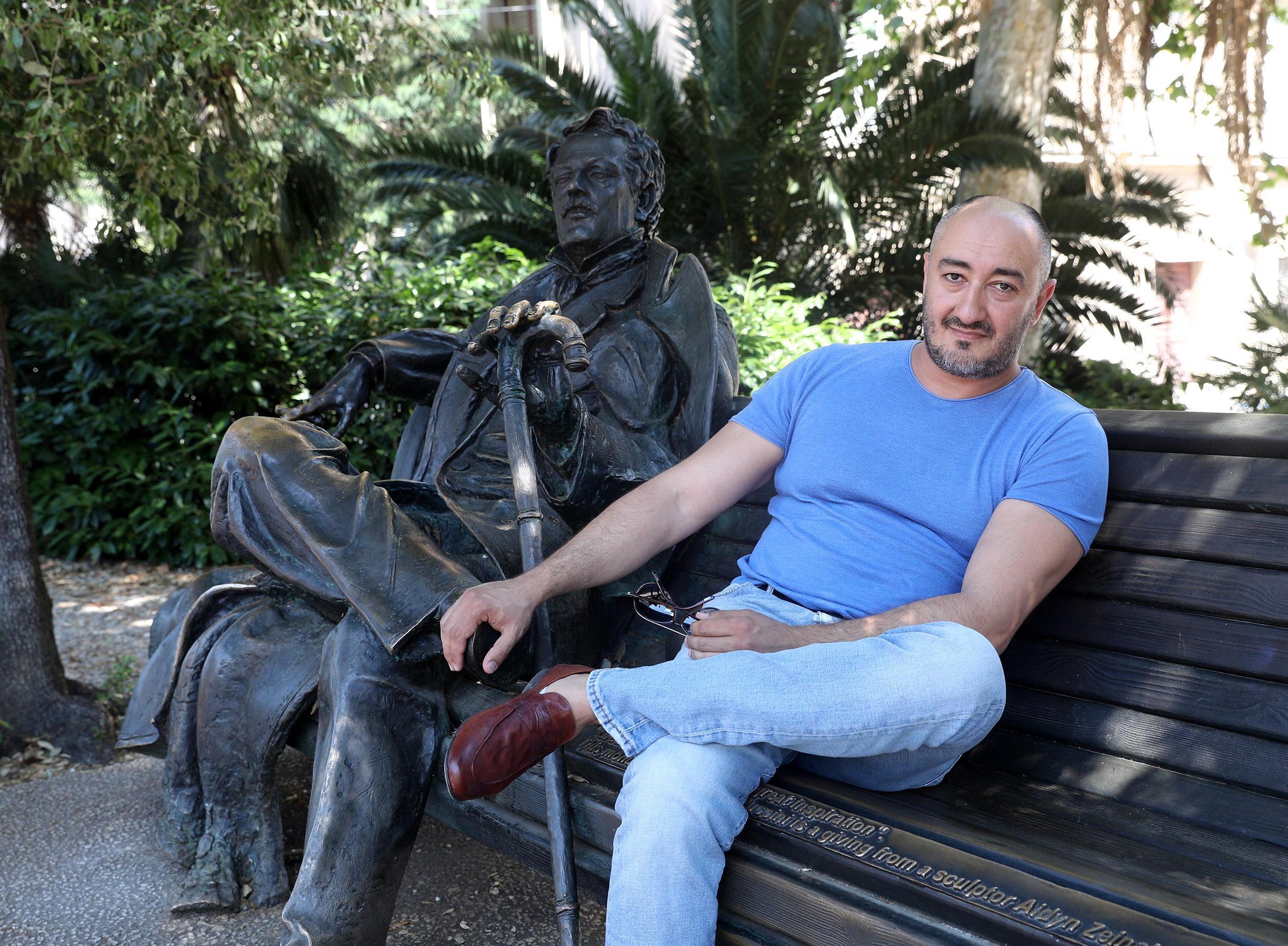 L’artista russo Aidyn Zeinalov accanto alla scultura che raffigura Giacomo Puccini seduto su una panchina nel viale Verdi (Foto Nucci)