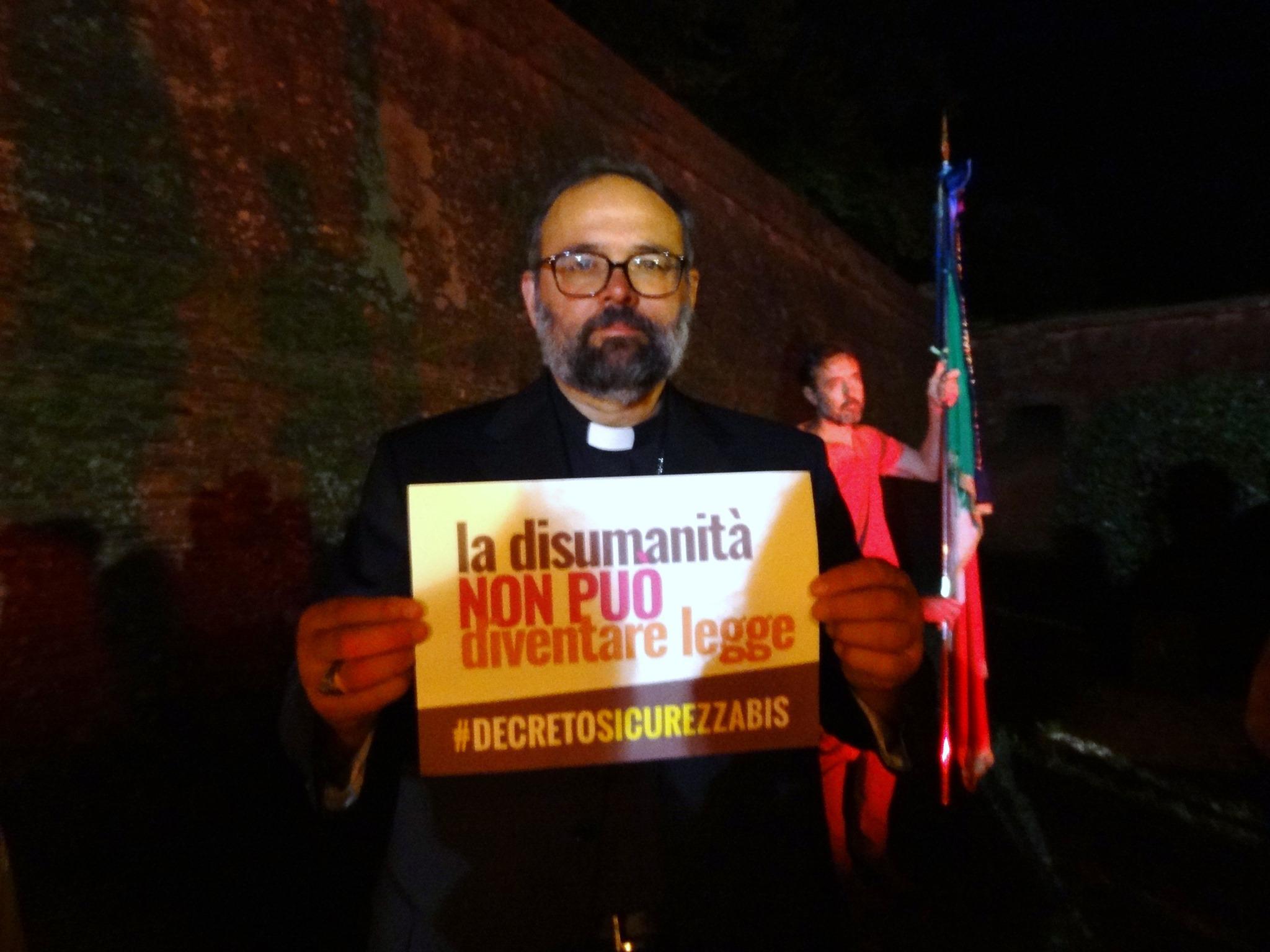 Il vescovo Paolo Giulietti con il cartello contro il decreto sicurezza bis