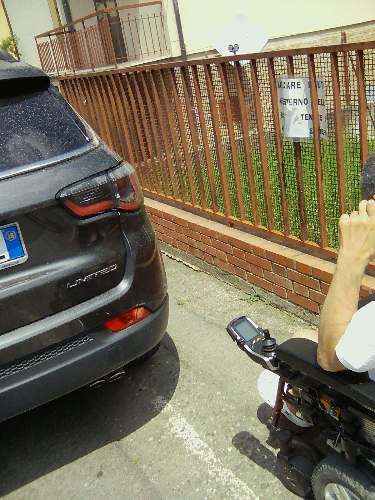 Il disabile alle prese con un'auto che gli impedisce il passaggio con la sua carrozzina