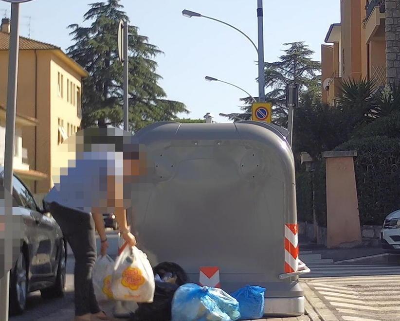 Una persona lascia i sacchetti della spazzatura accanto ai cassonetti informatizzati (che si aprono solo con la tessera magnetica) in via Tarquinia a Grosseto (foto del Comune di Grosseto)