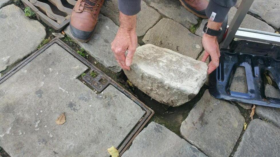 Una pietra è stata rimossa dal selciato del centro e “ricompare” sulla statua