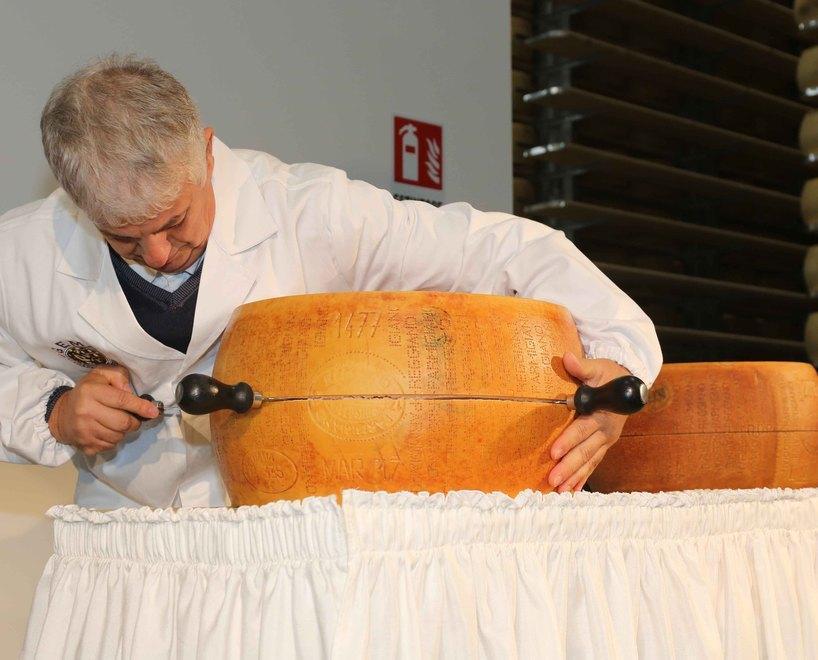 Un taglio della forma di Parmigiano Reggiano durante una manifestazione dentro a un magazzino