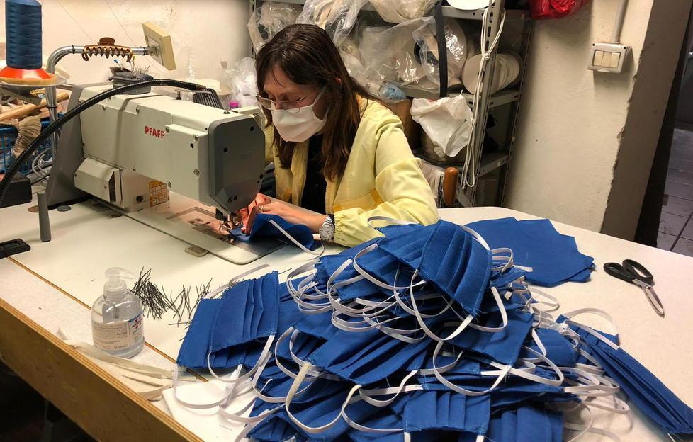 Un momento della lavorazione, che in questi giorni va avanti fino a tarda sera, e decine di mascherine già pronte