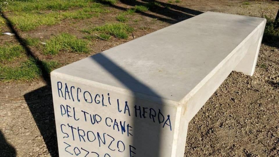 Una delle panchine imbrattata con la scritta contro i proprietari dei cani