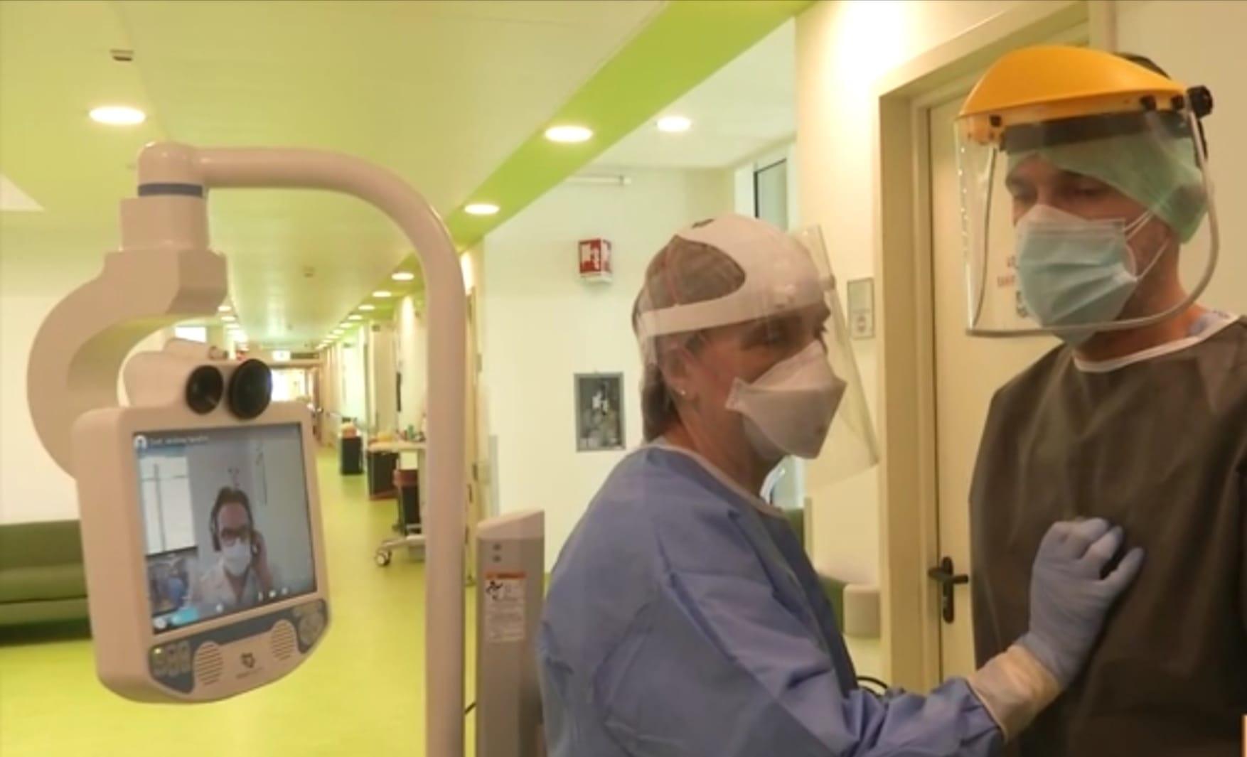 Due sanitari simulano l'auscultazione tramite uno stetoscopio che rimanda il segnale a un medico collegato da remoto, che segue la visita dallo schermo del robot