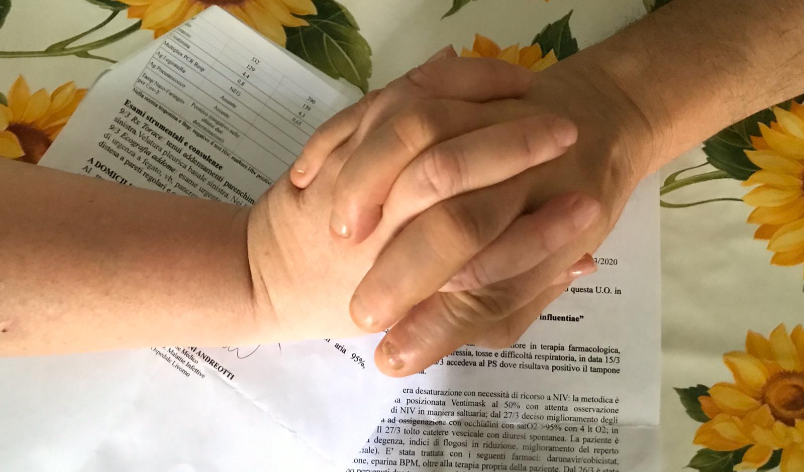 Le mani di Anna e Paolo (nomi di fantasia), si stringono forte: in secondo piano i fogli che certificano la loro guarigione dal coronavirus