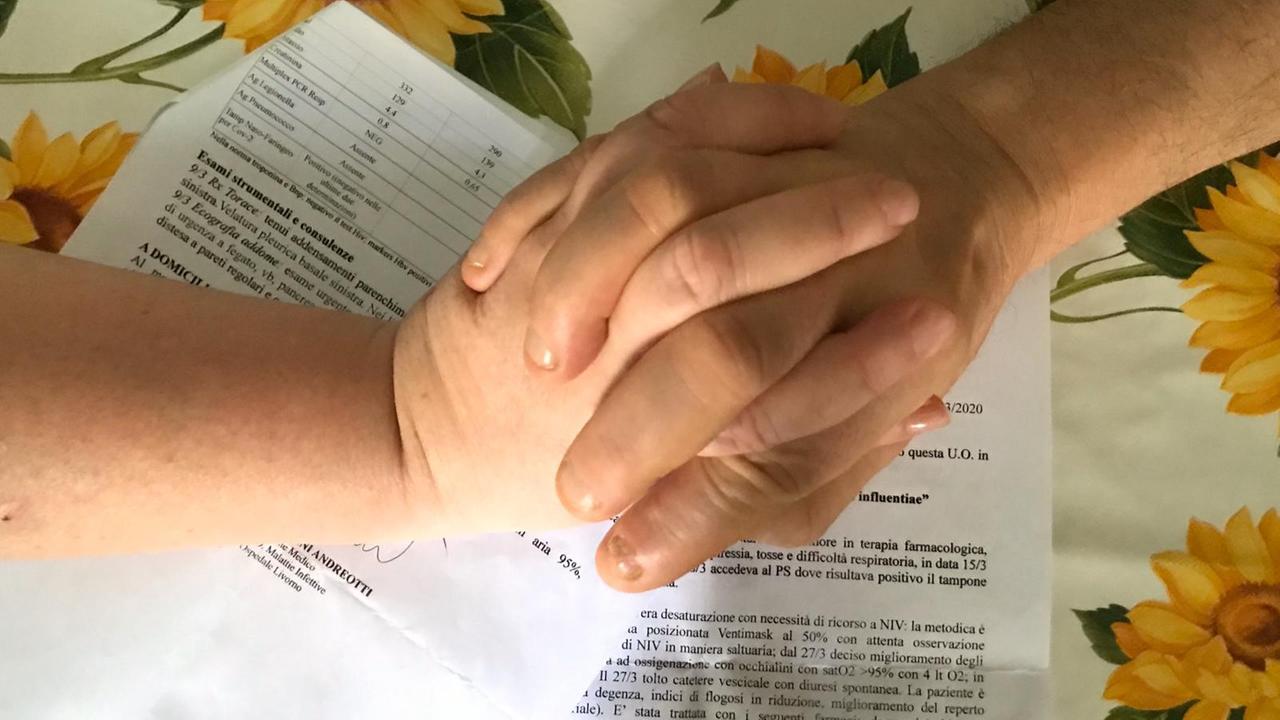 Le mani di Anna e Paolo (nomi di fantasia), si stringono forte: in secondo piano i fogli che certificano la loro guarigione dal coronavirus