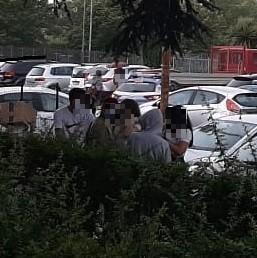 Un gruppo di ragazzi discute sull'epidosio ai giardini di Maliseti. Sullo sfondo una volante della polizia
