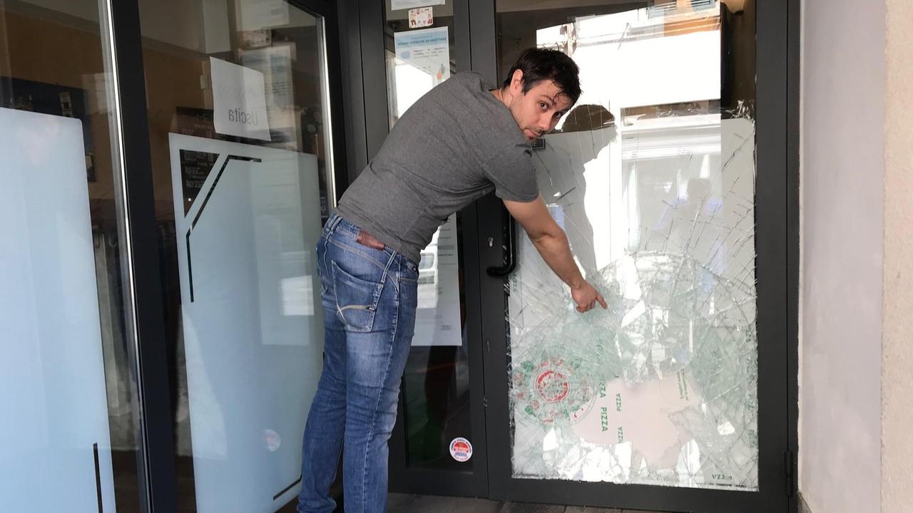 Andrea Fanciullacci mostra il vetro della porta d'ingresso della pizzeria infranto dai ladri