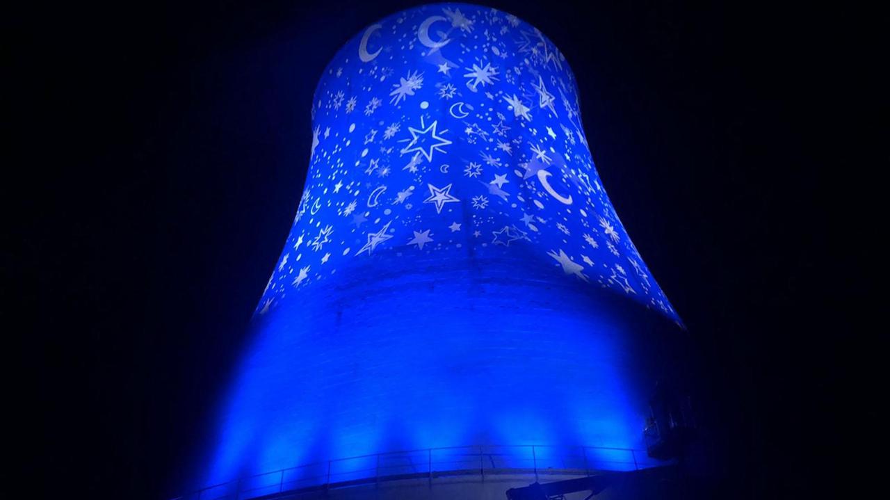 La torre refrigerante della centrale geotermica di Monterotondo Marittimo si accende di un elegantissimo manto di stelle e lune su sfondo blu