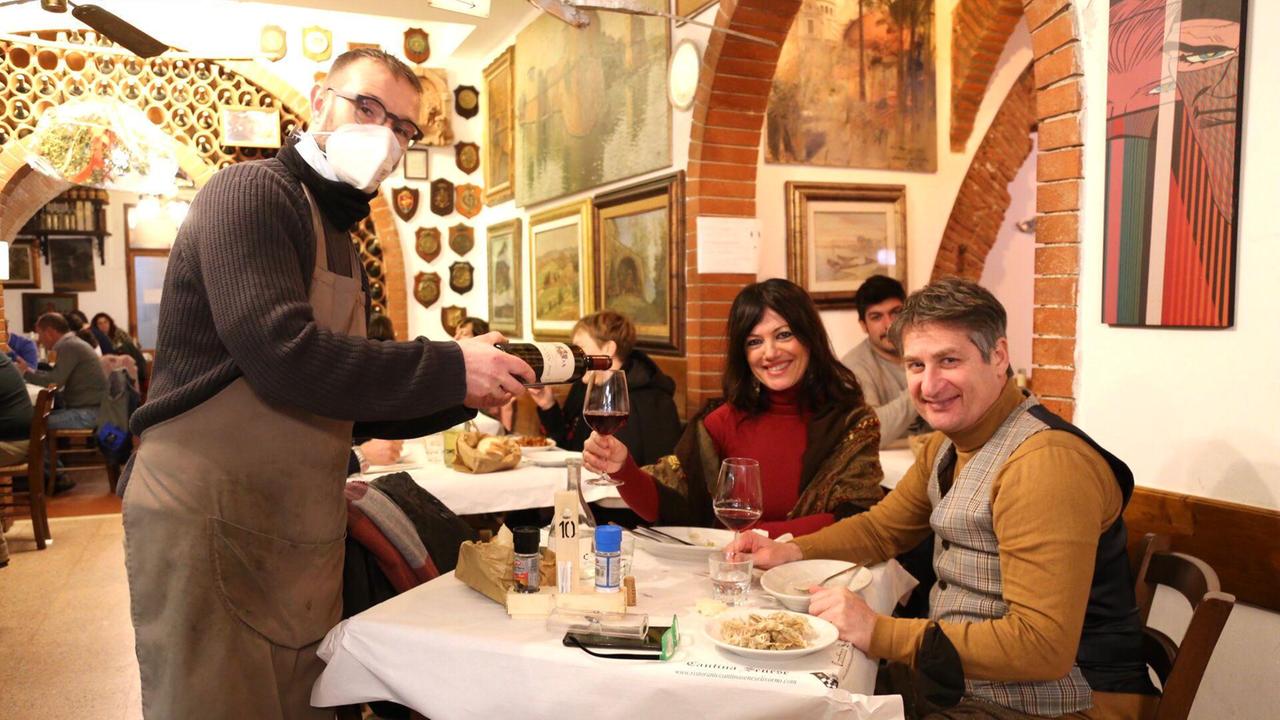 Il titolare della Cantina Senese insieme ad alcuni clienti sorridenti seduti a un tavolo del ristorante per il pranzo della vigilia di San Valentino