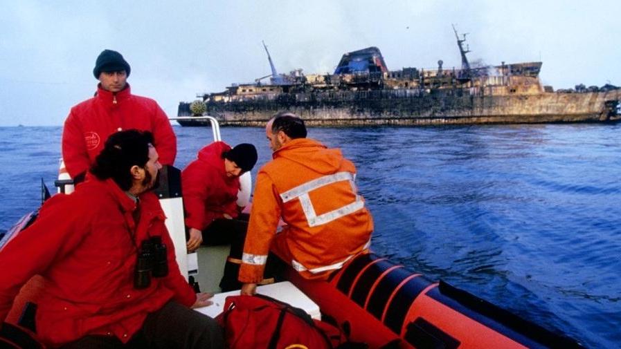Una squadra dei vigili del fuoco, a bordo di un gommone, la mattina dopo la sciagura davanti al relitto del Moby Prinbce annerito dal rogo