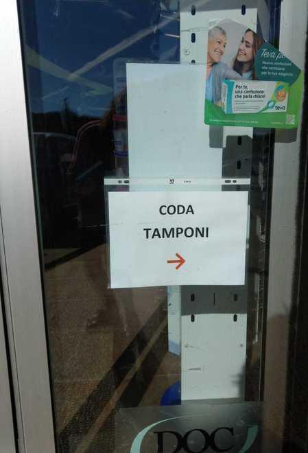 Un cartello che indica la "coda per i tamponi" all'ingresso di una farmacia di Pisa