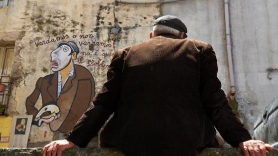 Un anziano davanti a un murale a Orgosolo
