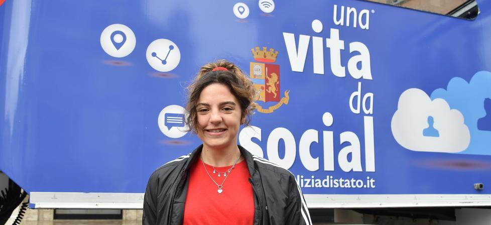 Ambra Sabatini davanti al poster della polizia postale a Grosseto