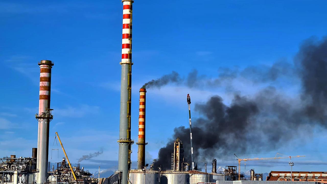 Le ciminiere della raffineria Eni a Stagno e, sullo sfondo, la nube di fumo nero che martedì pomeriggio si alzava dall’impianto danneggiato dal rogo (Franco Silvi)