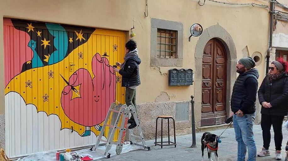 Un’artista disegna sulla saracinesca di una bottega di via Oberdan, nel quartiere delle Capanne, sotto gli occhi di due passanti