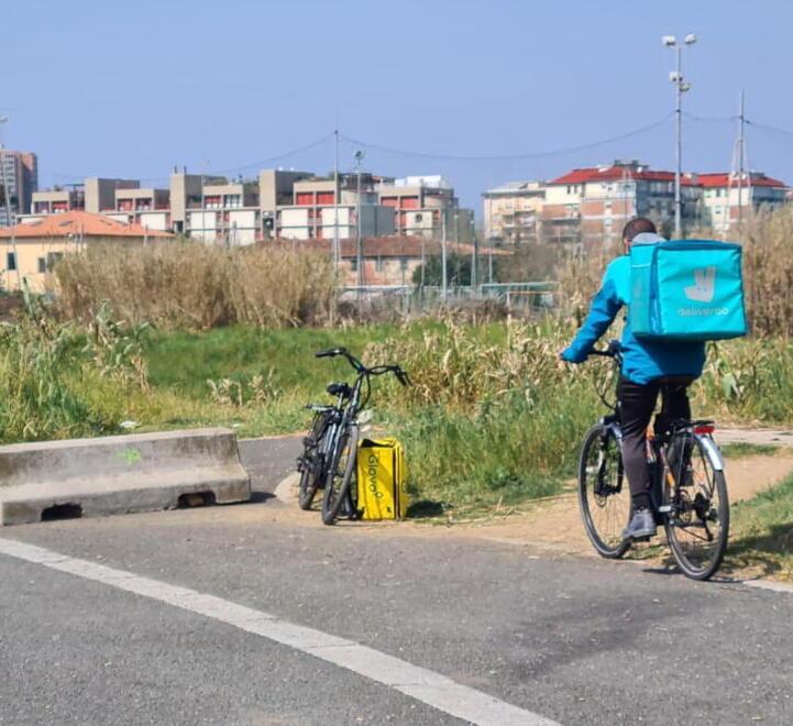 Un rider Deliveroo e una bici con lo zaino targato Glovo dietro al McDonald’s di Levante