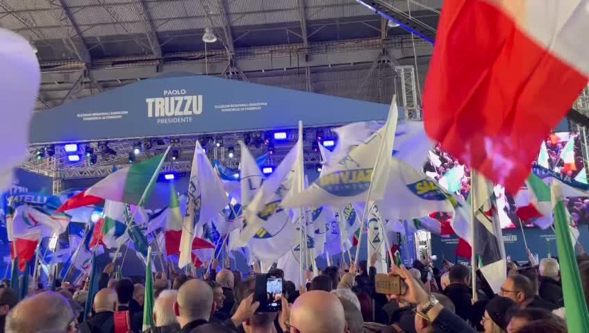 Una distesa di bandiere di Fratelli d'Italia e una folla di persone attendono l'arrivo di Giorgia Meloni alla Fiera di Cagliari